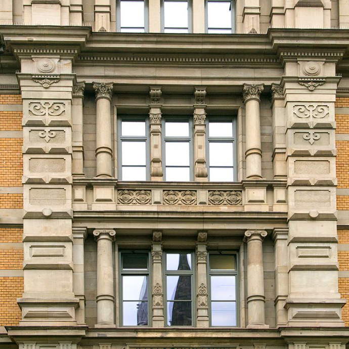 Detail einer historischen Fassade mit verzierten Steinrahmen, Säulen und Ornamentbändern. Kombination aus Naturstein und gelbem Klinker im Stil des 19. Jahrhunderts.