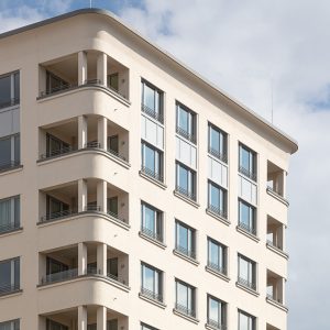 Nahaufnahme einer modernen Gebäudefassade mit abgerundeten Balkonecken und großen Fenstern in symmetrischer Anordnung.